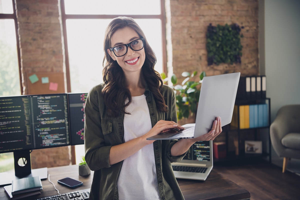 cheerful female programmer standing while holding a laptop