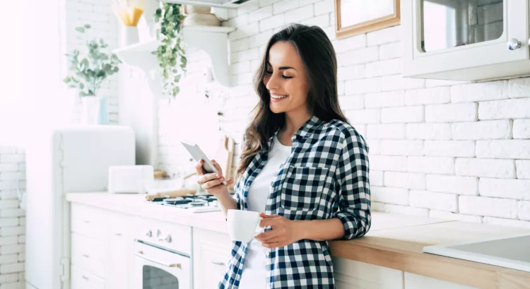 Cute smiling woman is using smart phone in the kitchen
