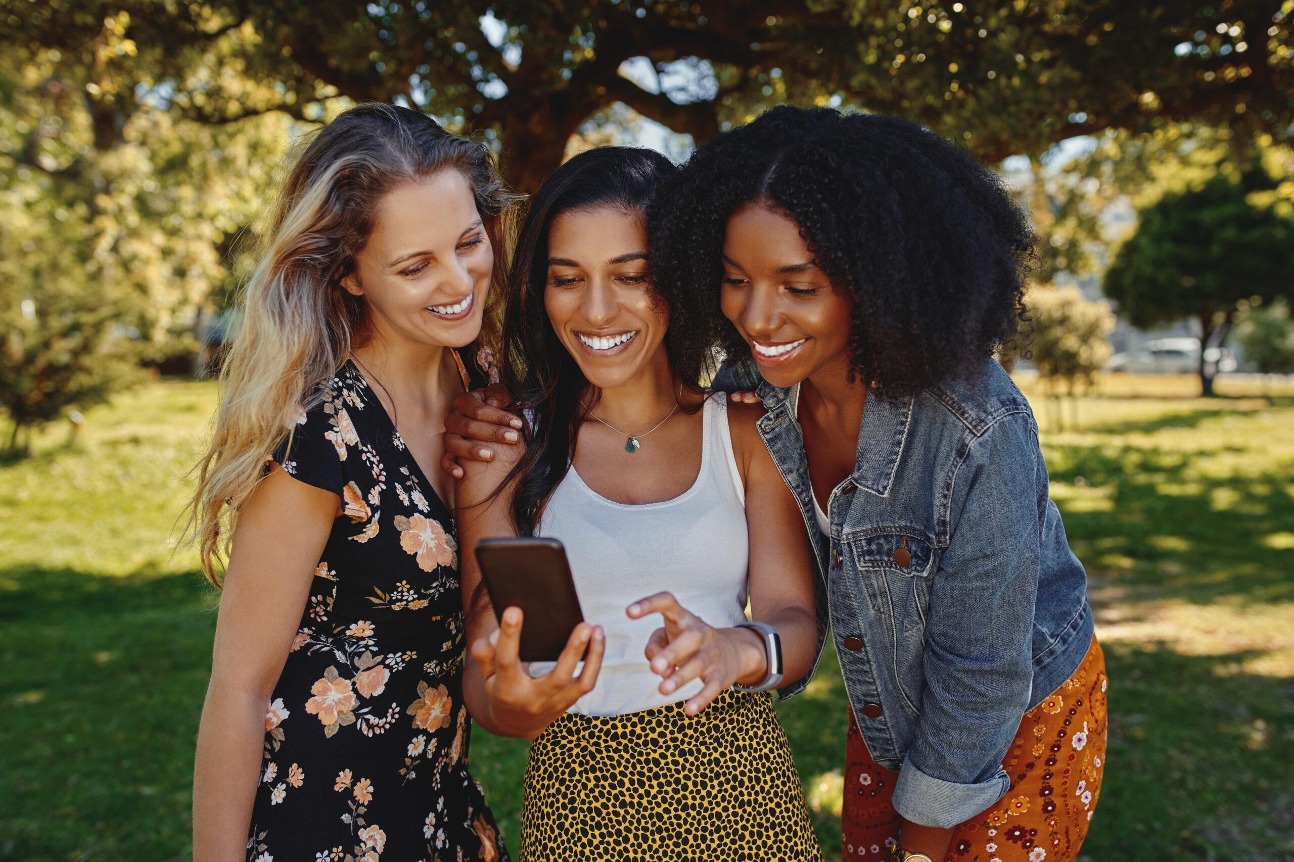 A group of young multiracial mixed race friends looking at one smart phone in the park