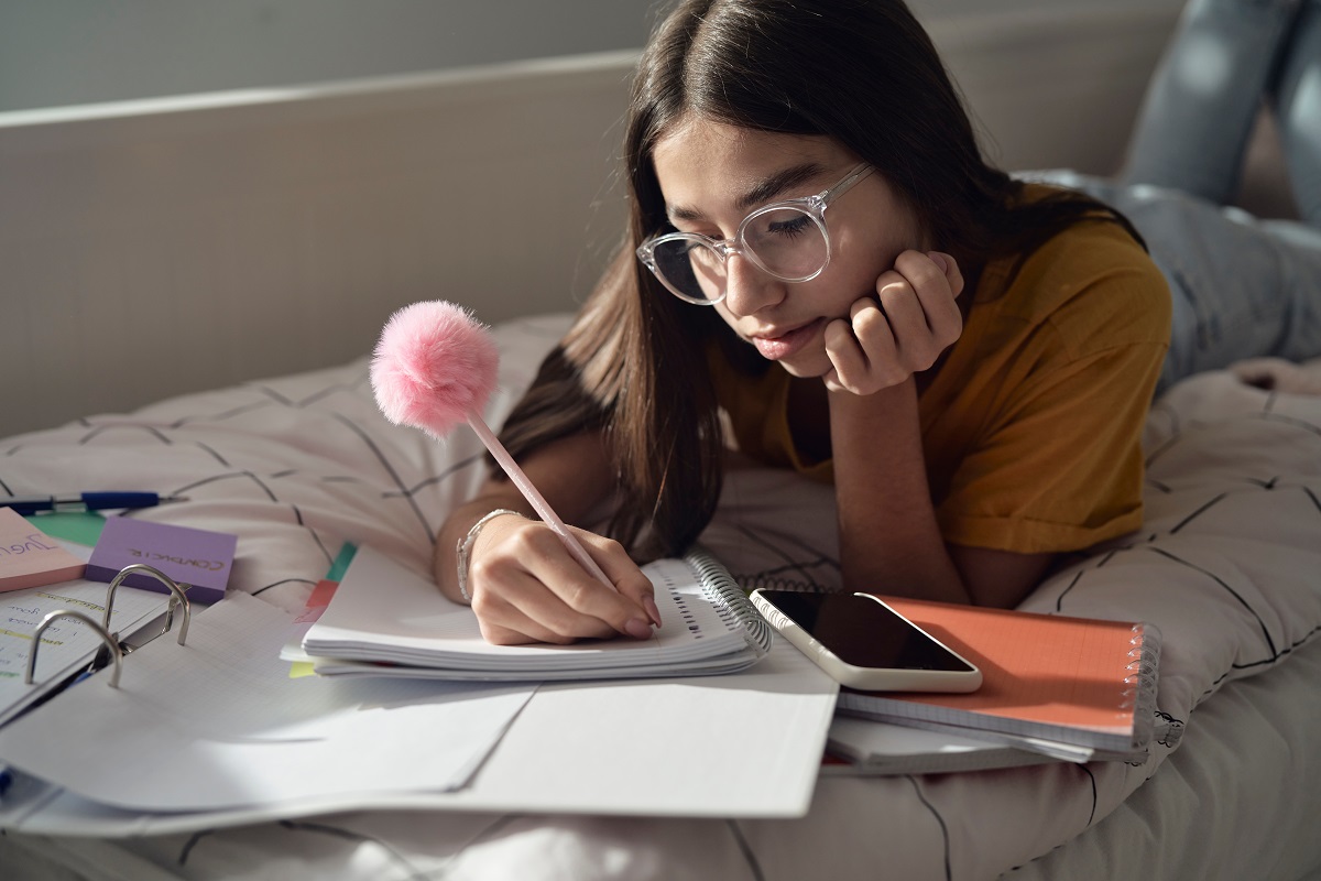 teenage girl doing homework in bed