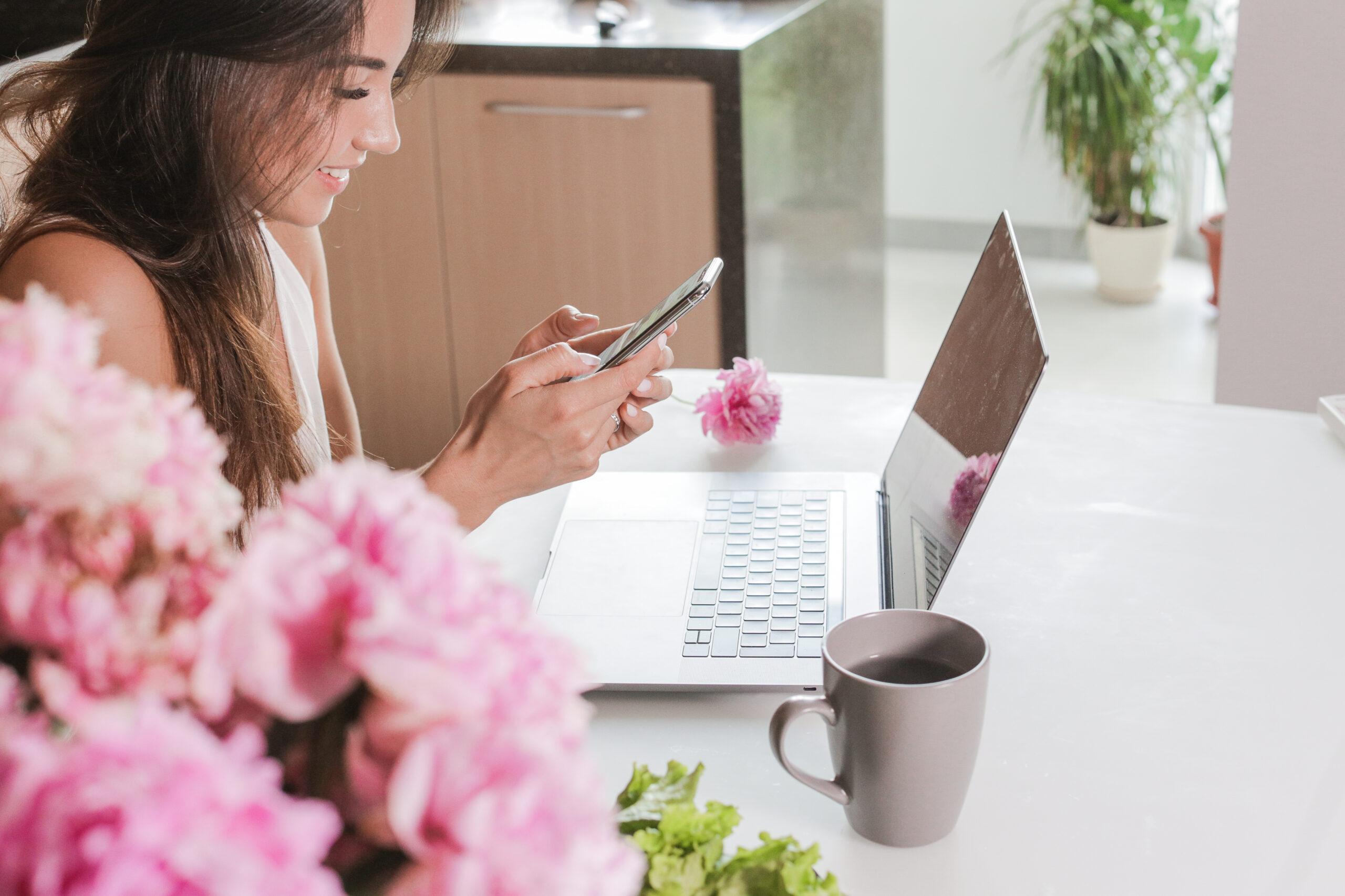 brunette girl typing a message in the phone next to the laptop.