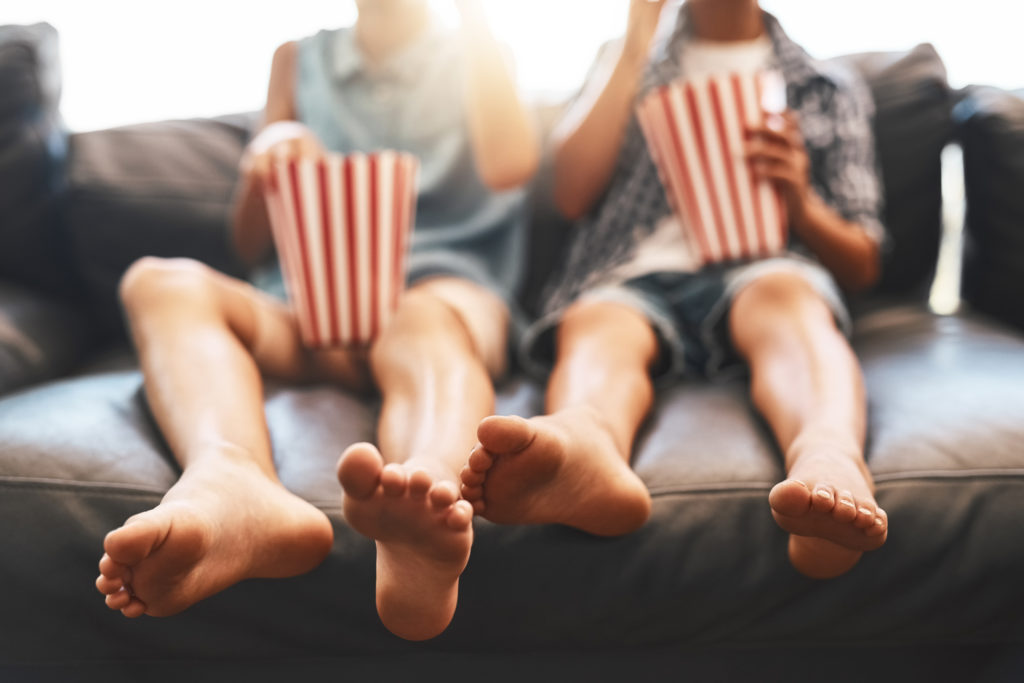 It's movie time, brother and sister eating popcorn while watching a movie at home.