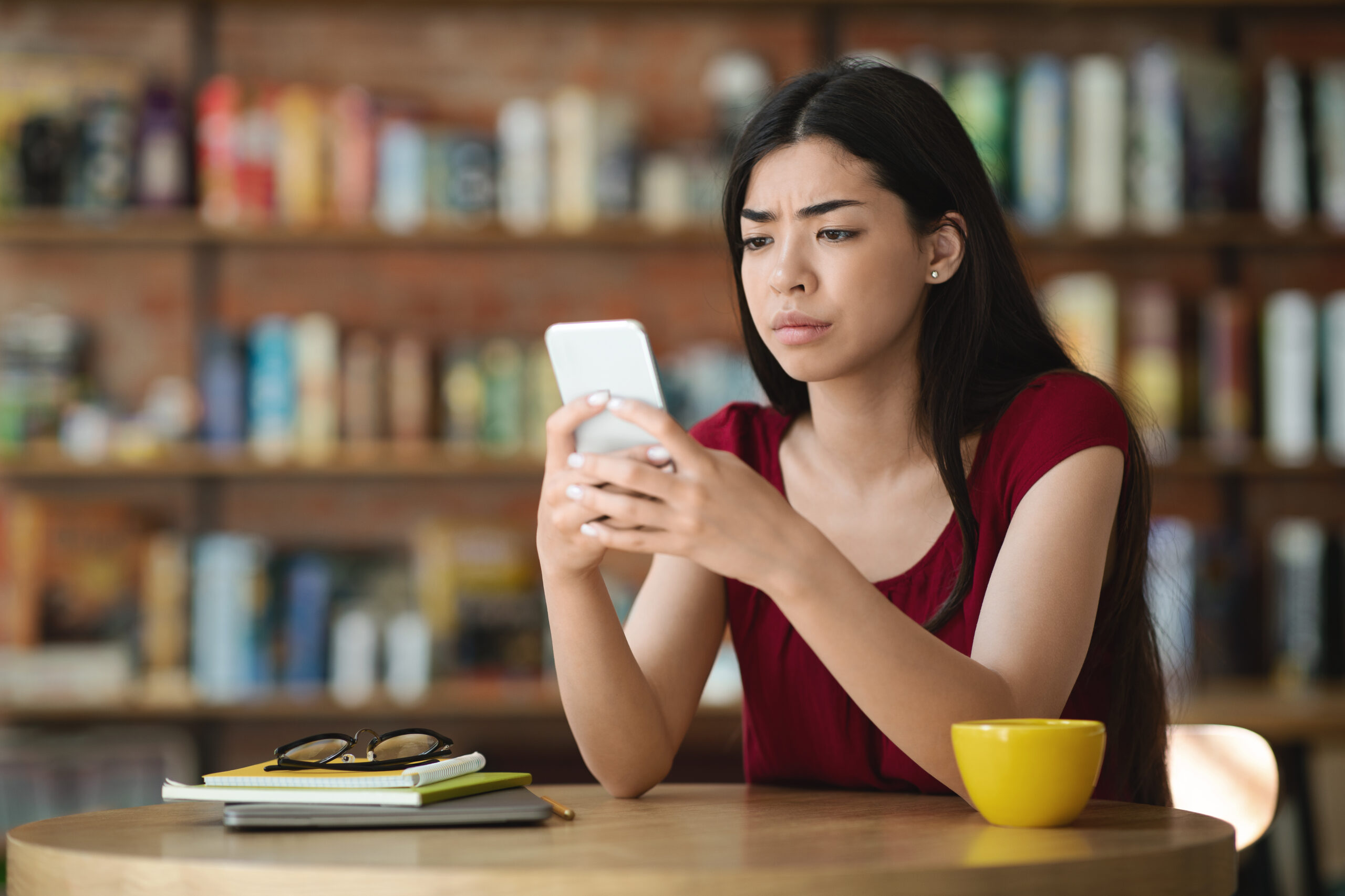 Bad News. Upset Asian Girl Looking At Smartphone Screen In Cafe, Reading Message