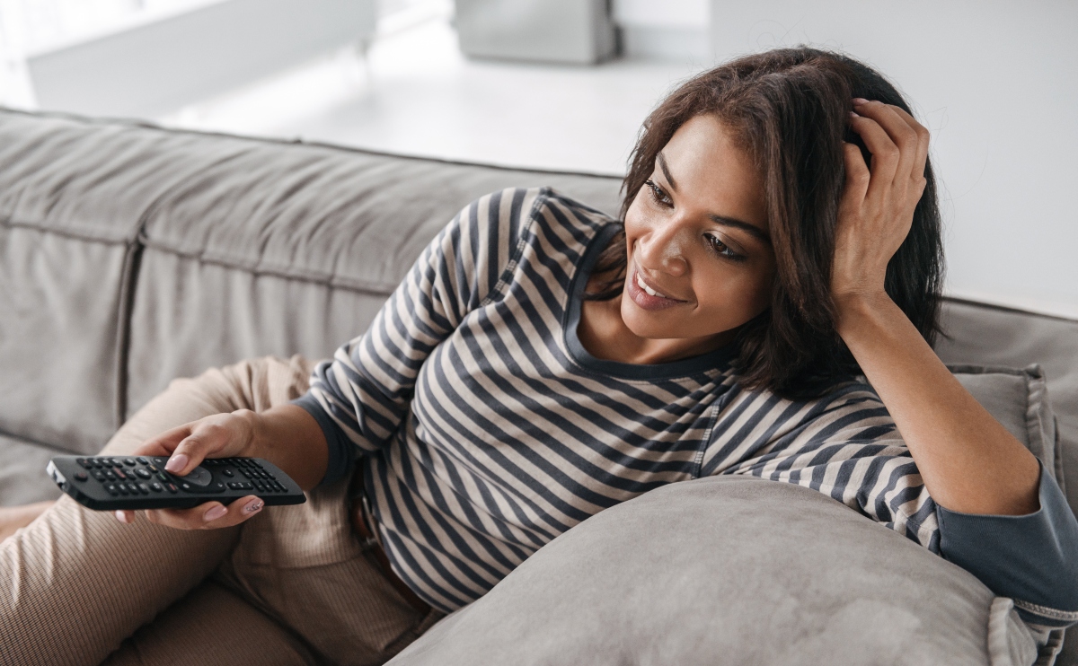 Attractive woman with TV remote watching the Person of Interest series and curious about how they force pair cell phones.