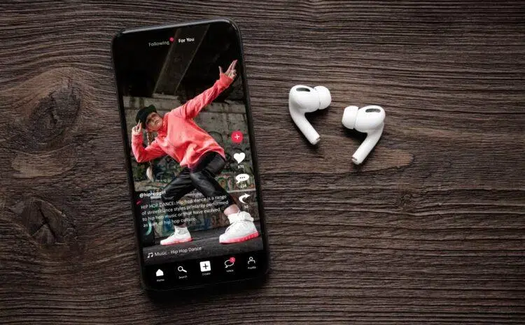 Phone showing a video of a dancing boy, ear pods at the side on a wooden table