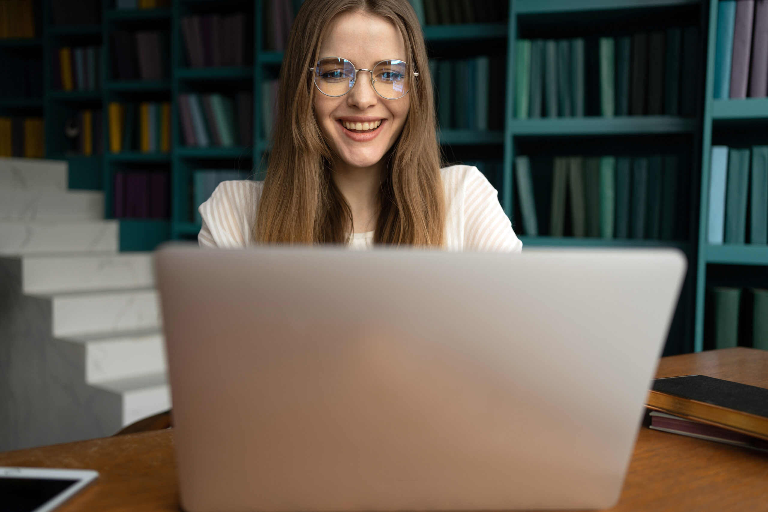 A female student with glasses studying in the library with her laptop