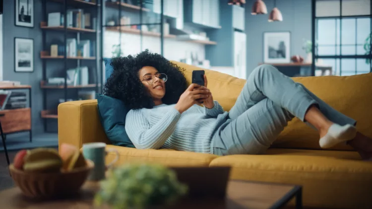 Happy beautiful woman using smartphone in cozy living room