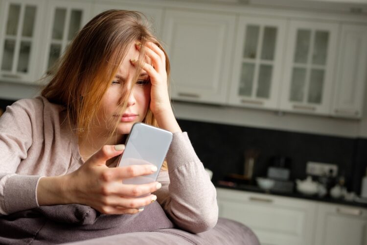 woman holding her phone looking stressed and frustrated