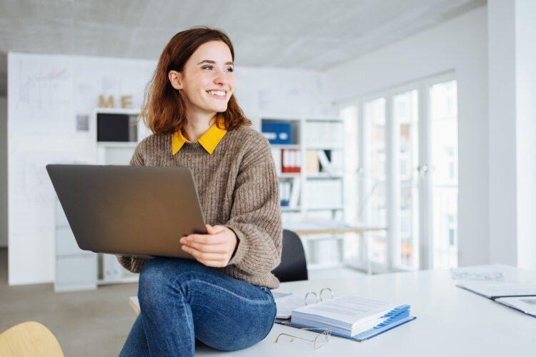 young cheerful woman sitting on a desk with laptop in her hands