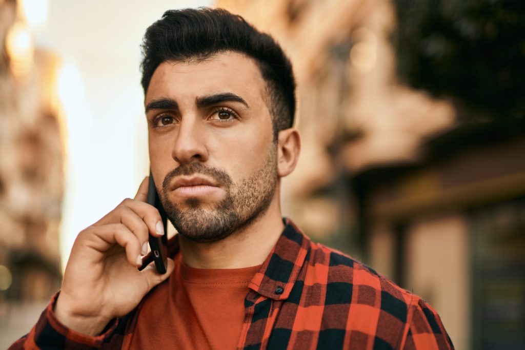 Young hispanic man with serious expression talking on the smartphone outdoor.