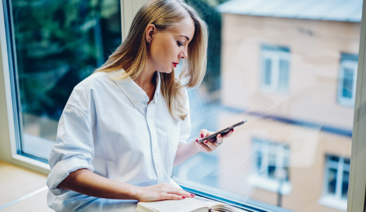 Serious woman using smartphone near window