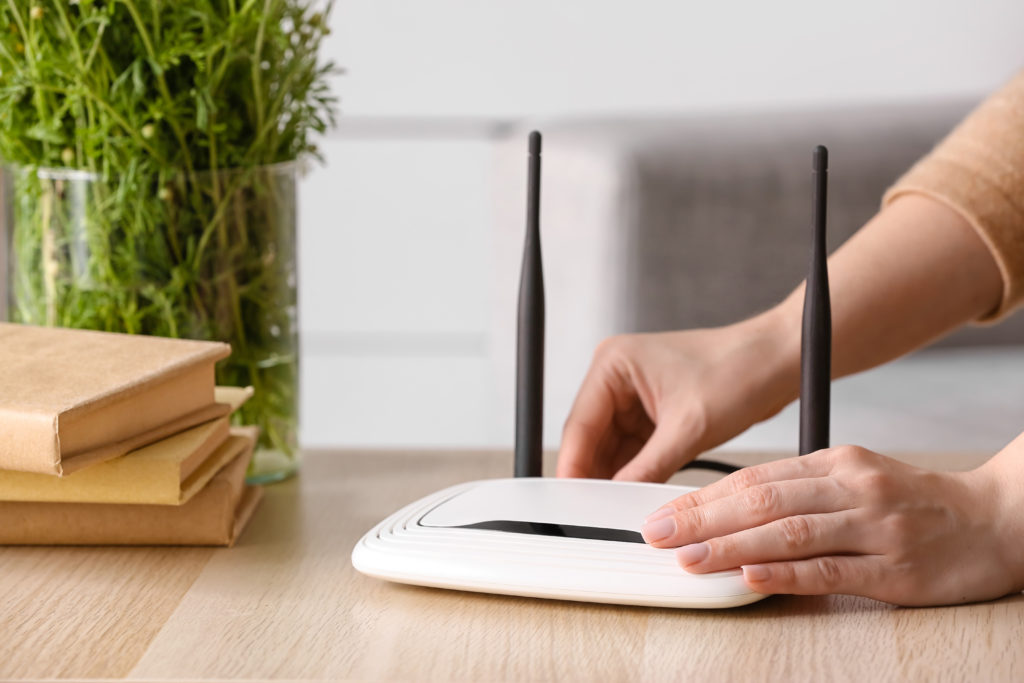 Woman plugging ethernet wire into wi-fi router on table in room