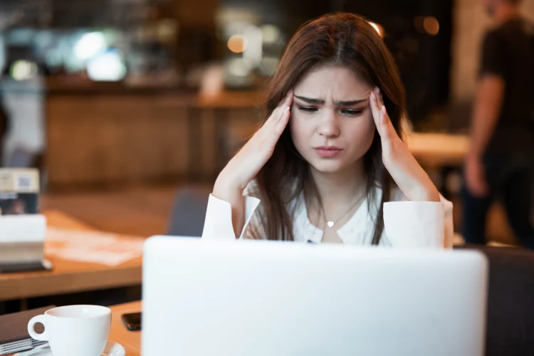 young beautiful woman looks stressed in front of laptop at a cafe.
