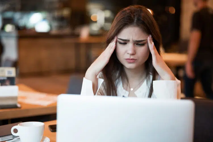 young beautiful woman looks stressed in front of laptop at a cafe.
