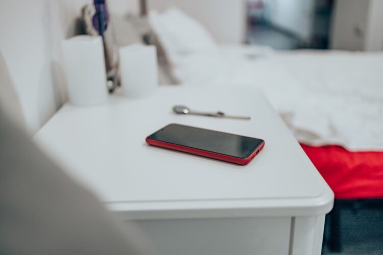 Black smartphone in a red case on the bedside table. 