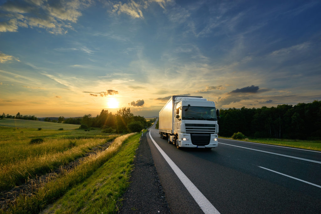 White cargo truck driving through a rural landscape after customs clearance completed.