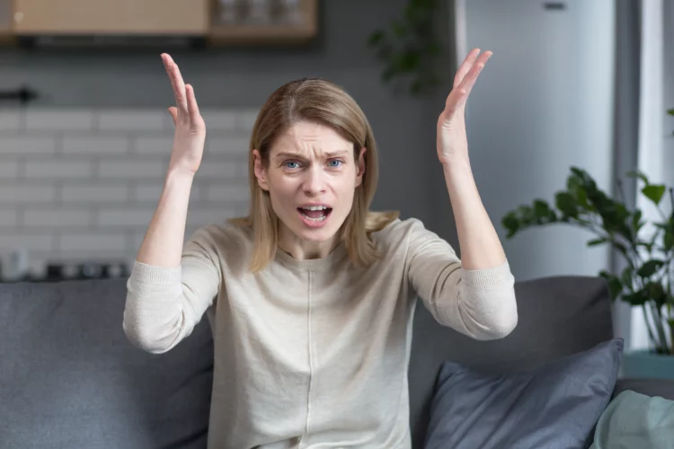 Angry and frustrated woman gesturing with hands while sitting on sofa at home