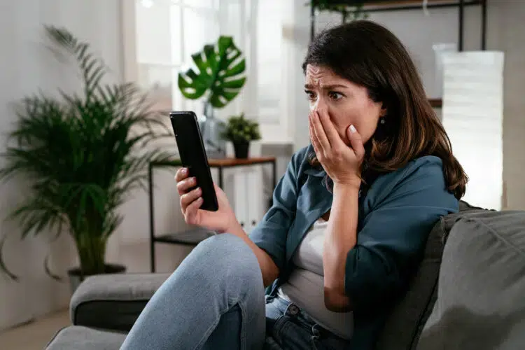 Sad woman sitting on the couch, using the phone.