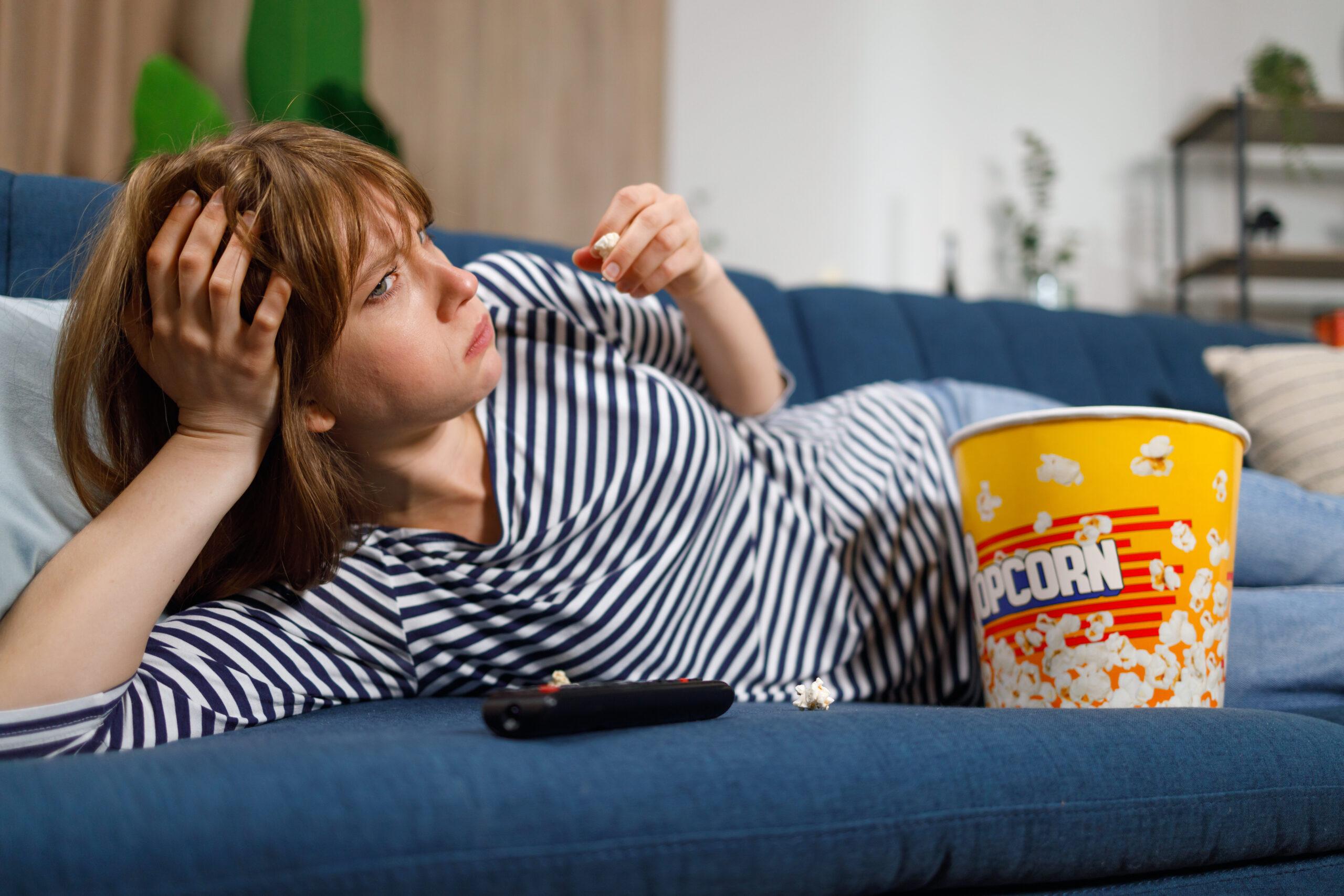 Woman watching a boring movie on TV and eating popcorn