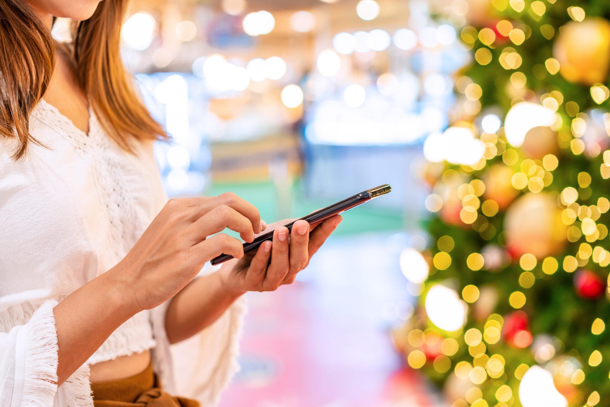 Young woman using smart phone and looking for online shopping promotion on social media  during the Christmas season at the mall
