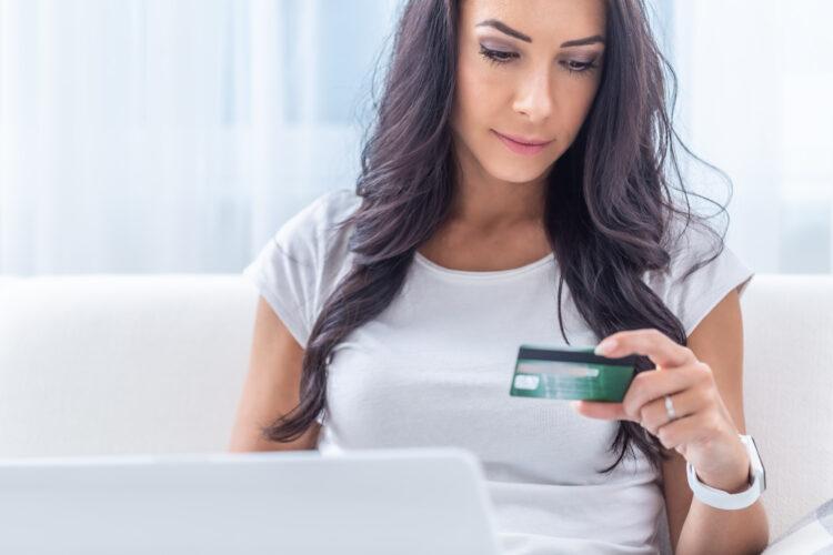 Brunette young woman looking at the credit card doing online payment at home