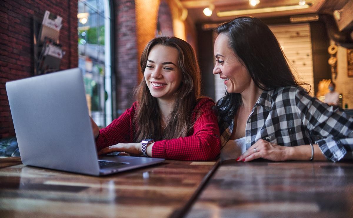 Happy smiling mother and daughter watching together video content on a laptop and having good time together in a coffee shop