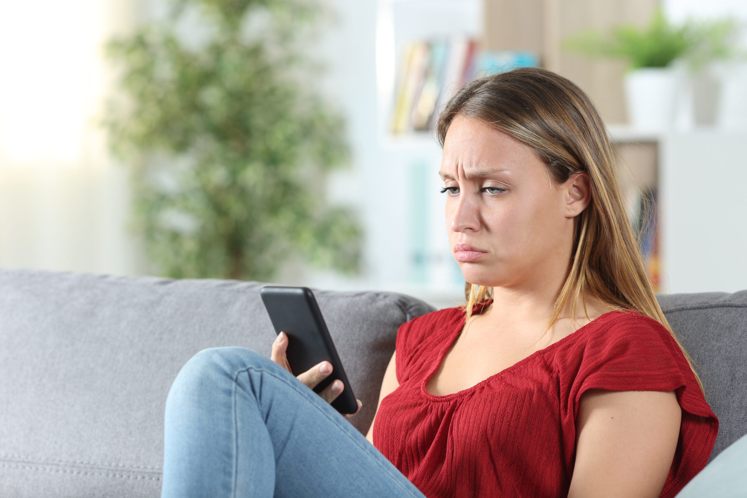Confused woman after looking at her phone in the couch