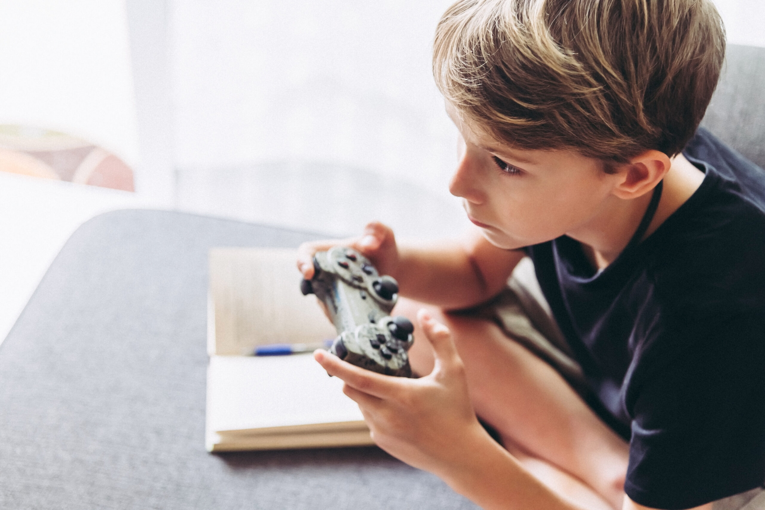 Blond child playing video games instead of studying sitting home
