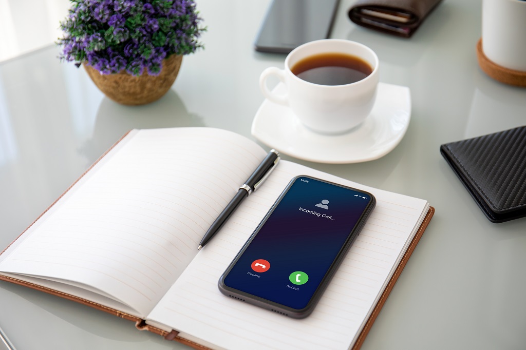 telefoon met inkomende oproep op het scherm bovenop een notebook in kantoor.