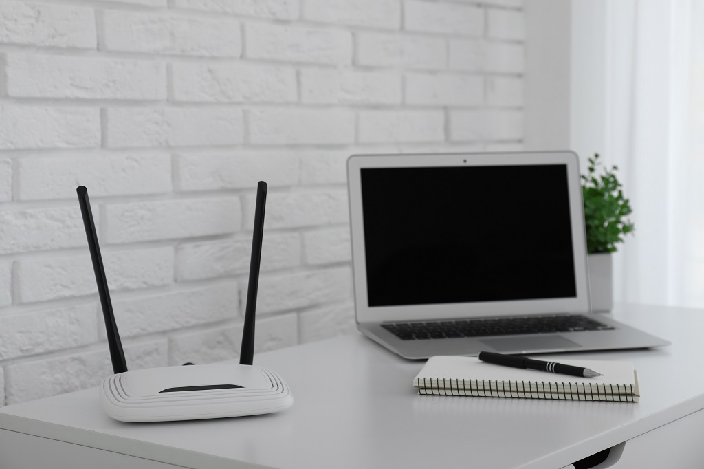 Router, modern laptop and notebook on white table indoors.