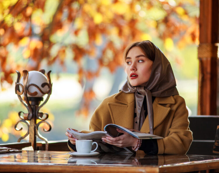 Luxurious young woman in retro fashion style reading at a cafe.