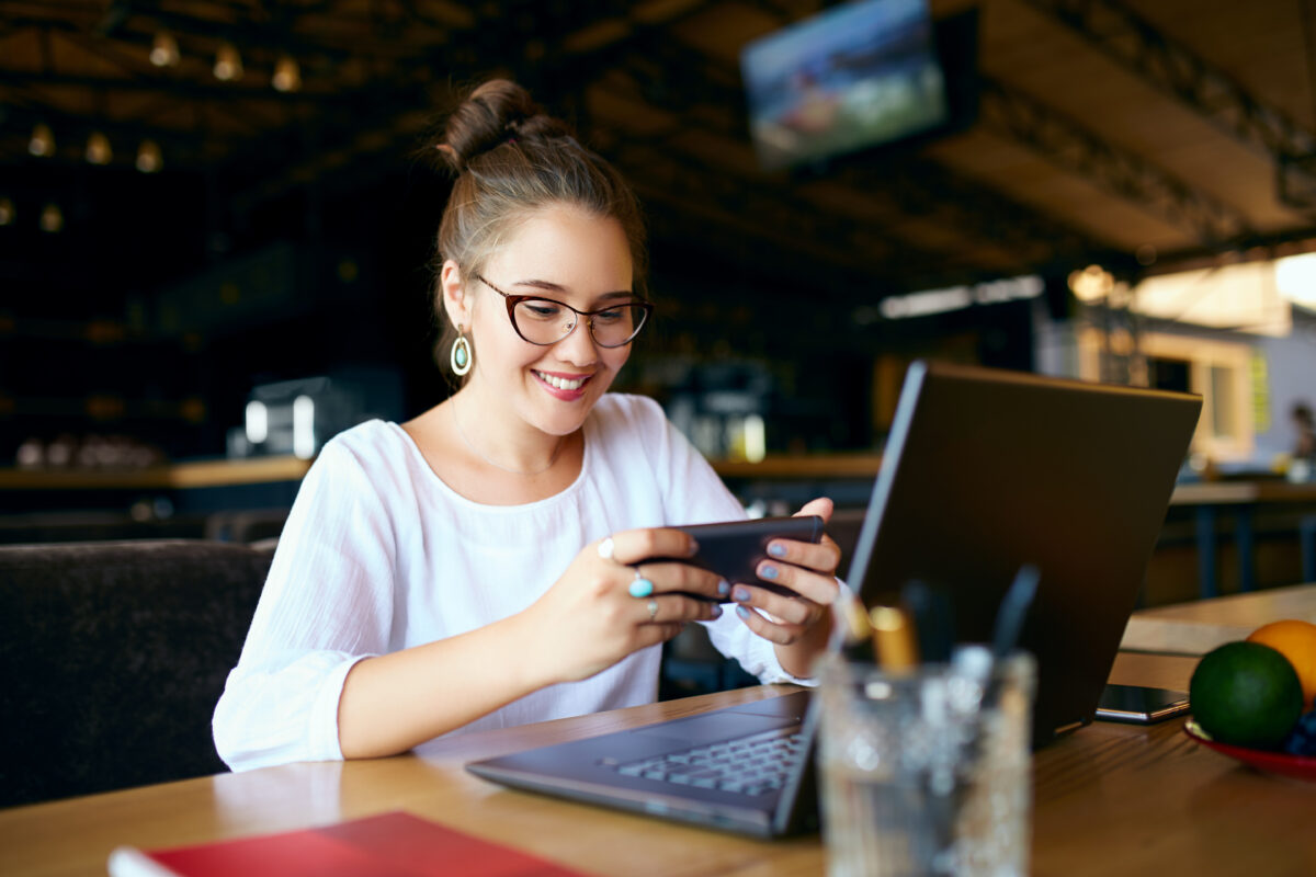 Woman using cellphone and laptop at a cafe.