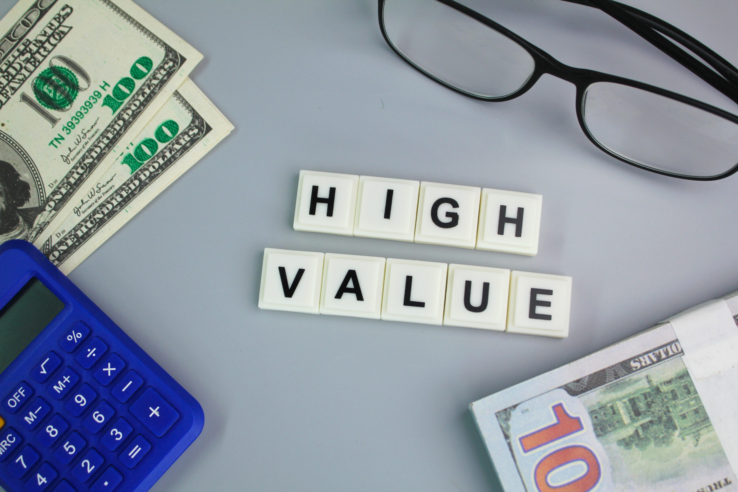 the word HIGH VALUE on wood tiles on table with 100 dollar bills and calculator