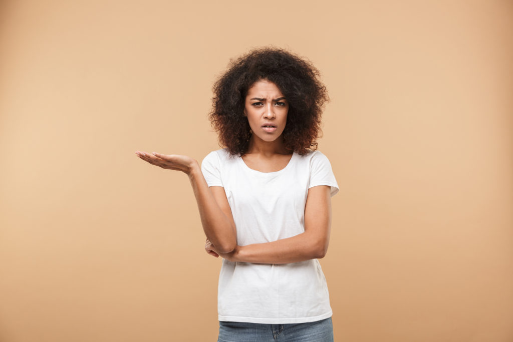 Portrait of a confused young african woman looking at camera isolated over beige background.