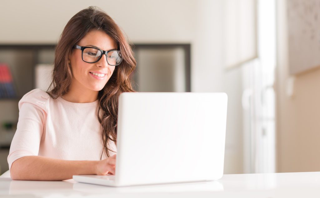 Woman in glasses using a white laptop.