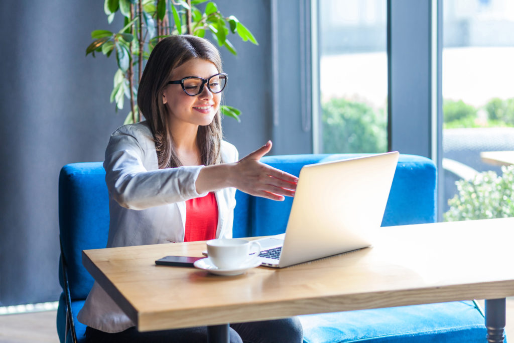 Woman giving a hand shake while having a video call on her laptop.