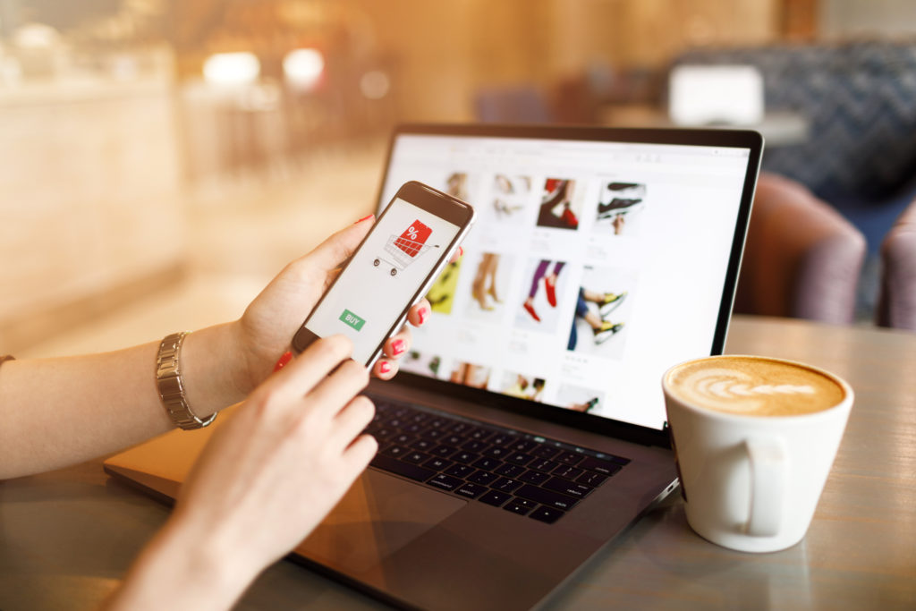 Woman using laptop and phone for online shopping.