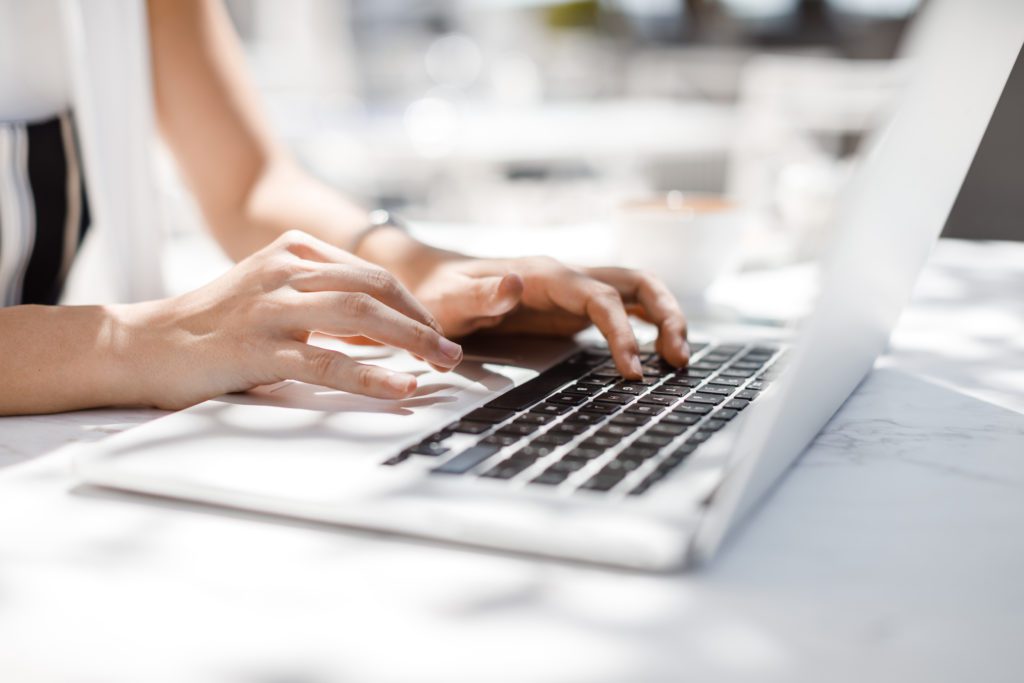 A woman working outdoors with white laptop.