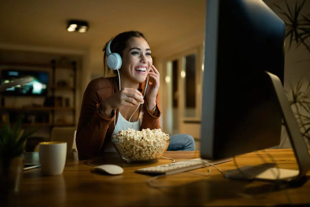 Young woman having fun while eating popcorn and watching movie on a computer.