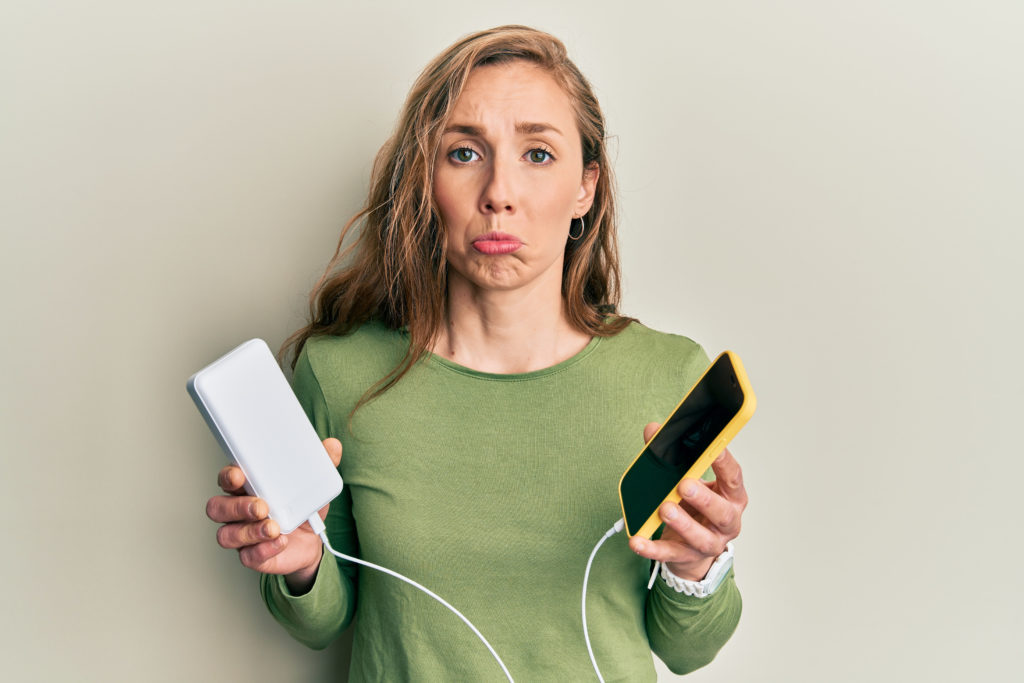 Woman with a sad expression while holding her phone and powerbank.