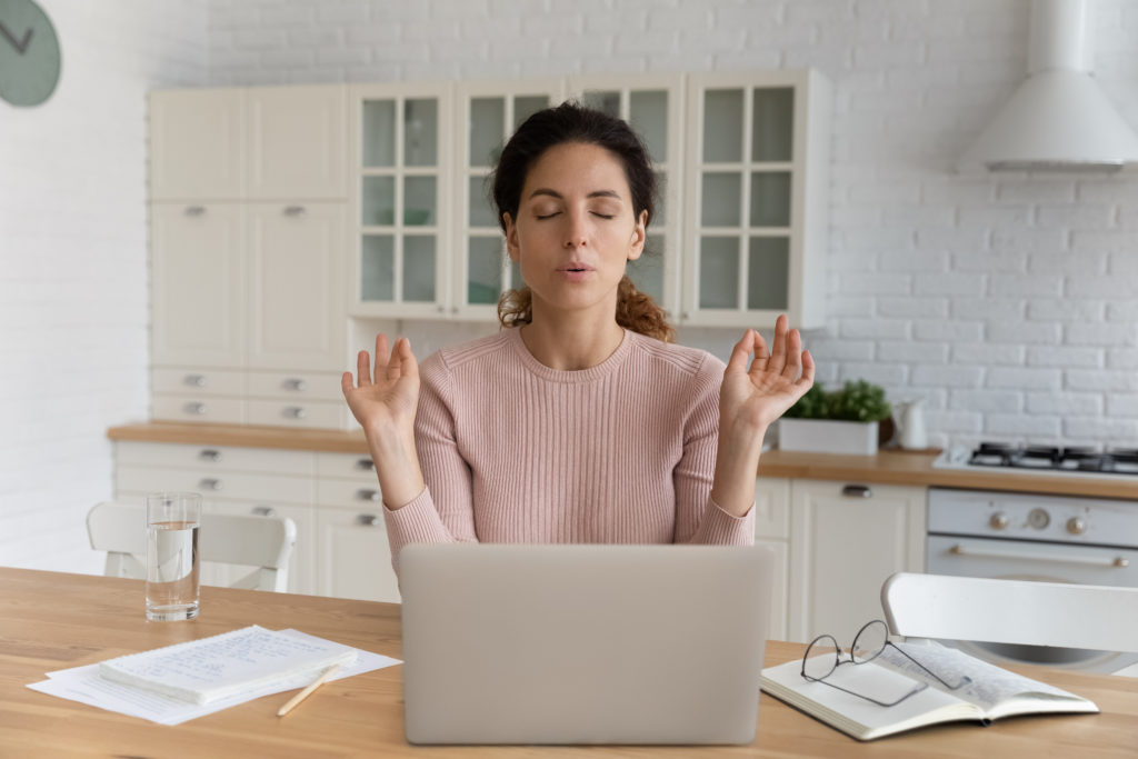 Woman stressed with paperwork in front of laptop.