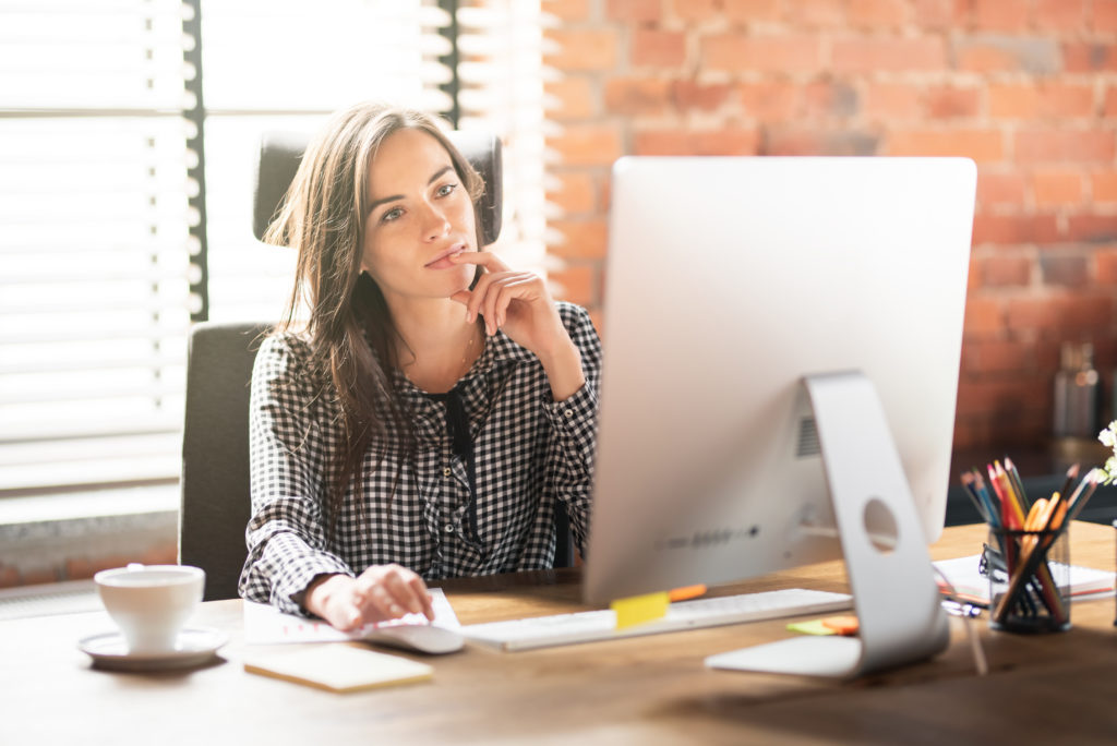 Woman thinking and working with big computer monitor at the office.