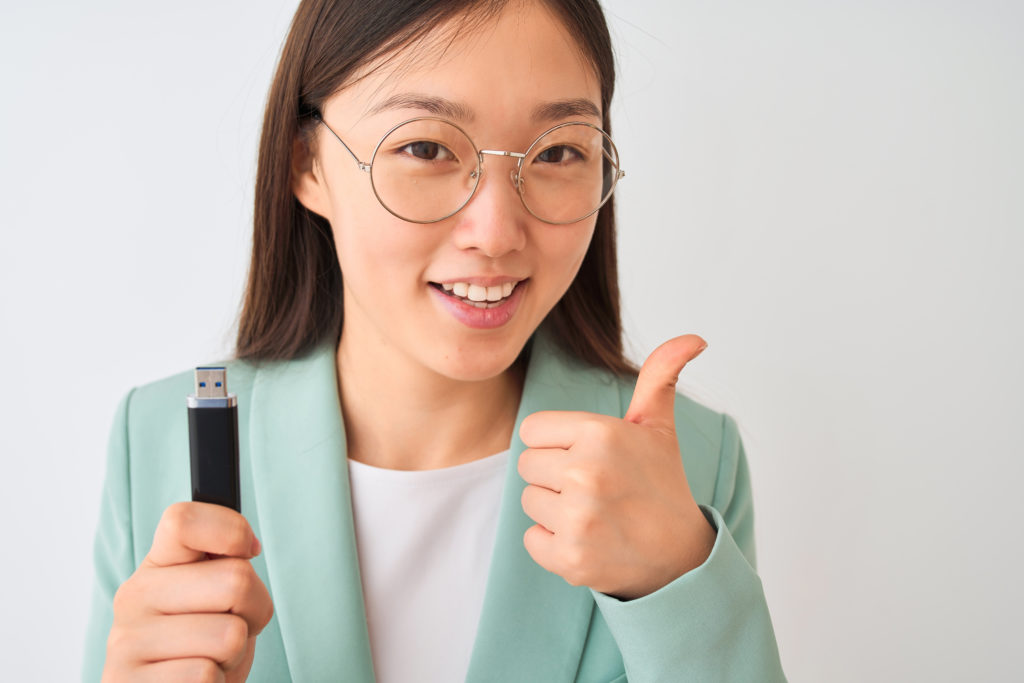 Young woman with USB flash drive, doing a thumbs up sign with her hand.