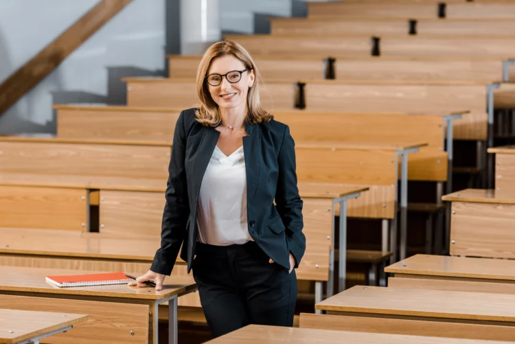Beautiful female university professor smiling, standing in the aisle of a large classroom.
