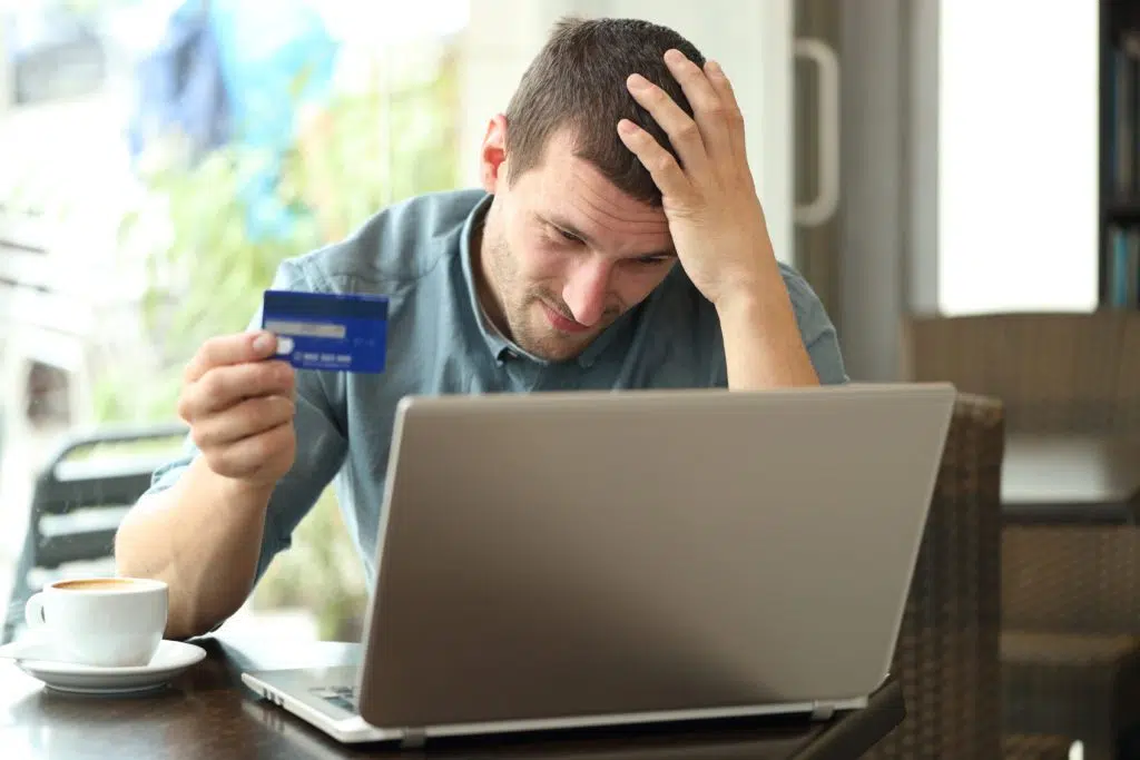 Worried man having a problem with his card, looking at his laptop.