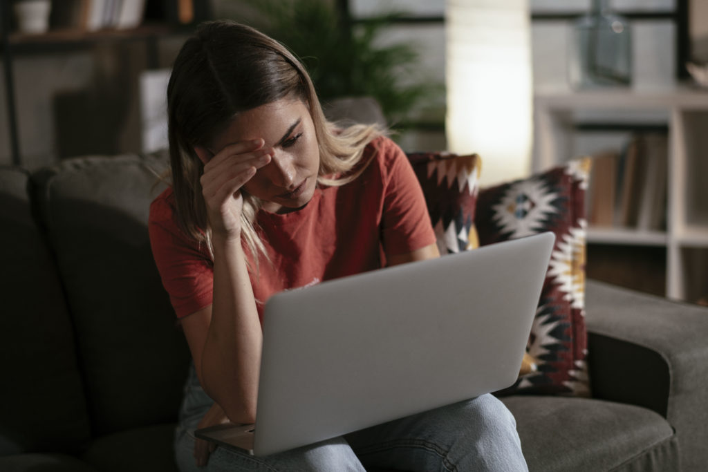 Worried and sad woman using her laptop inside the living room.