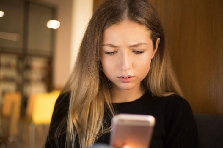 Confused young woman using mobile phone indoors