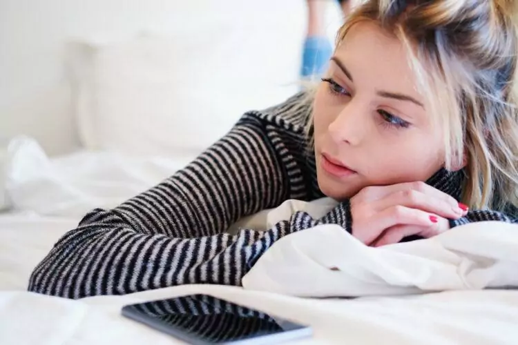 Disappointed sad woman and mobile phone laying on bed