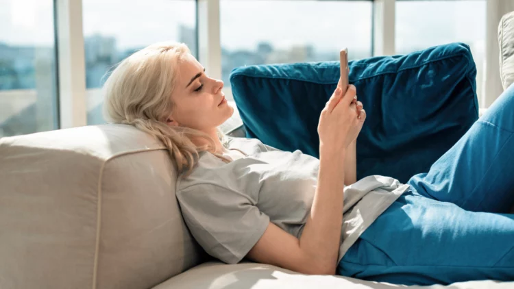 Young blonde woman lying on the sofa with smartphone