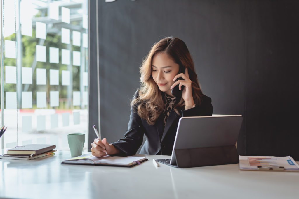 Young businesswoman talking on the phone while writing down on her notebook.